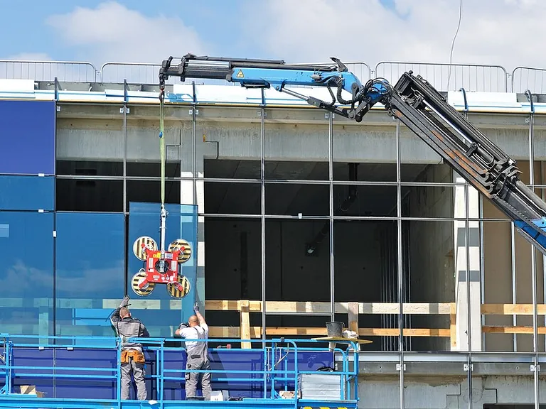 Glaserei Berlin bei der Montage großer Fassadengläser mit Kran und Vakuumsauger auf einer Baustelle.